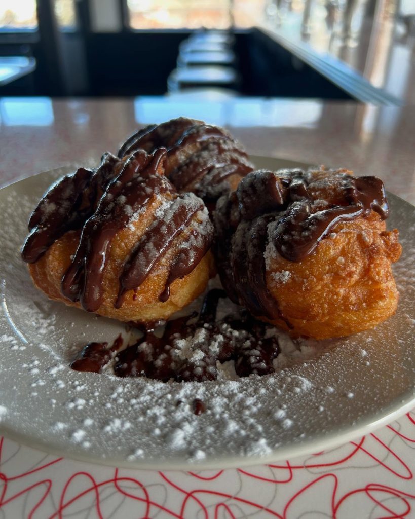 Golden pastries dusted with powdered sugar and drizzled with chocolate