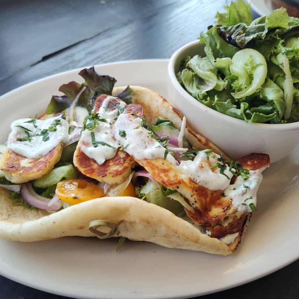 Pita with grilled cheese, vegetables, and creamy sauce alongside a green salad