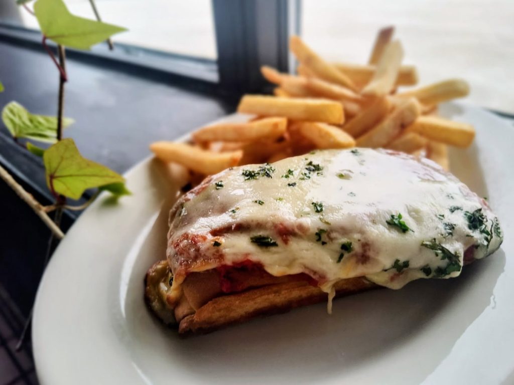 Open-faced sandwich covered in melted cheese and herbs beside French fries