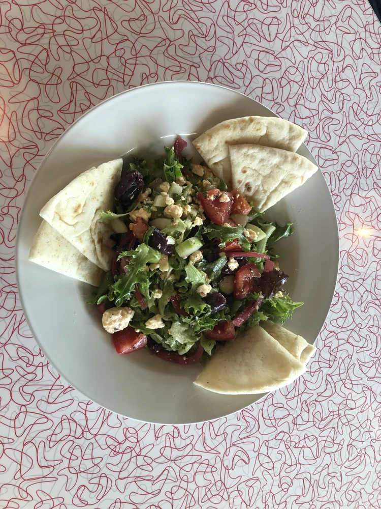 Mixed green salad with tomatoes, olives, cheese, and pita wedges